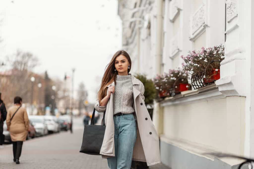 A beautiful young woman wearing a sweater and off white trench coat
