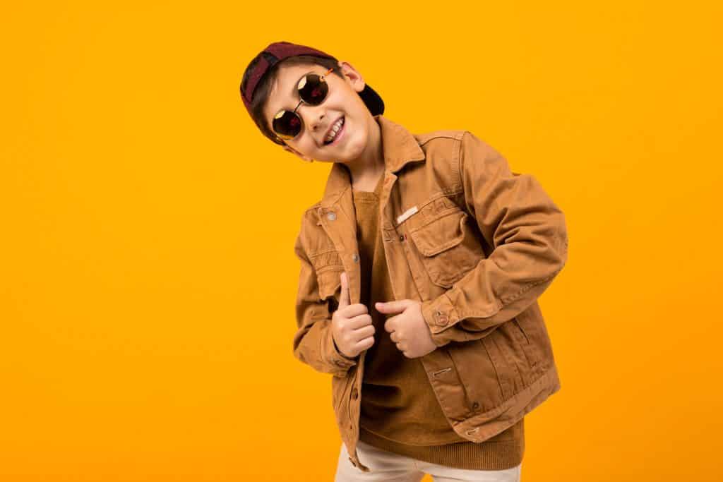 A kid wearing a brown colored denim jacket on a yellow background