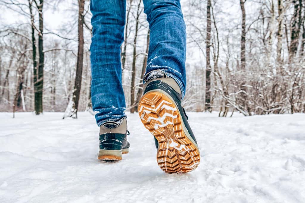 Man's legs in black with orange boots walking in the snow