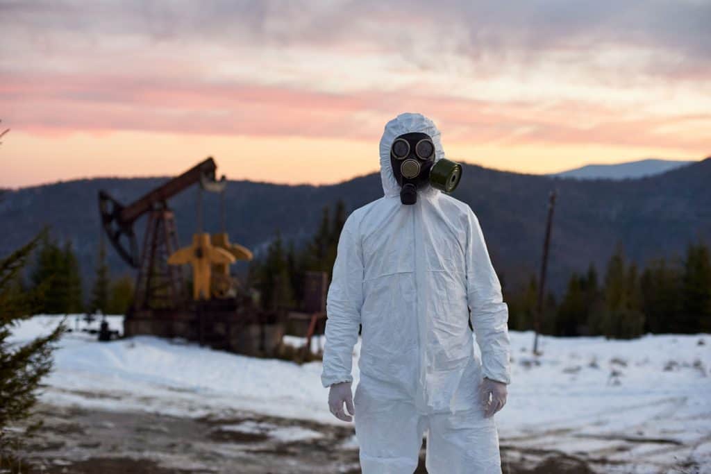 Scientist wearing white coverall, gloves and a gas mask working in oil field in mountainous region