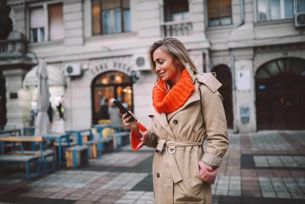 Woman wearing a brown trench coat while looking at her phone