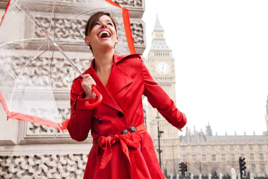 Photo of a happy young woman in a bright red trench coat and umbrella