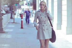 A beautiful blonde woman wearing an off white trench coat while talking on the phone, Should A Trench Coat Be Buttoned? [And How To Style One Without Looking Creepy]