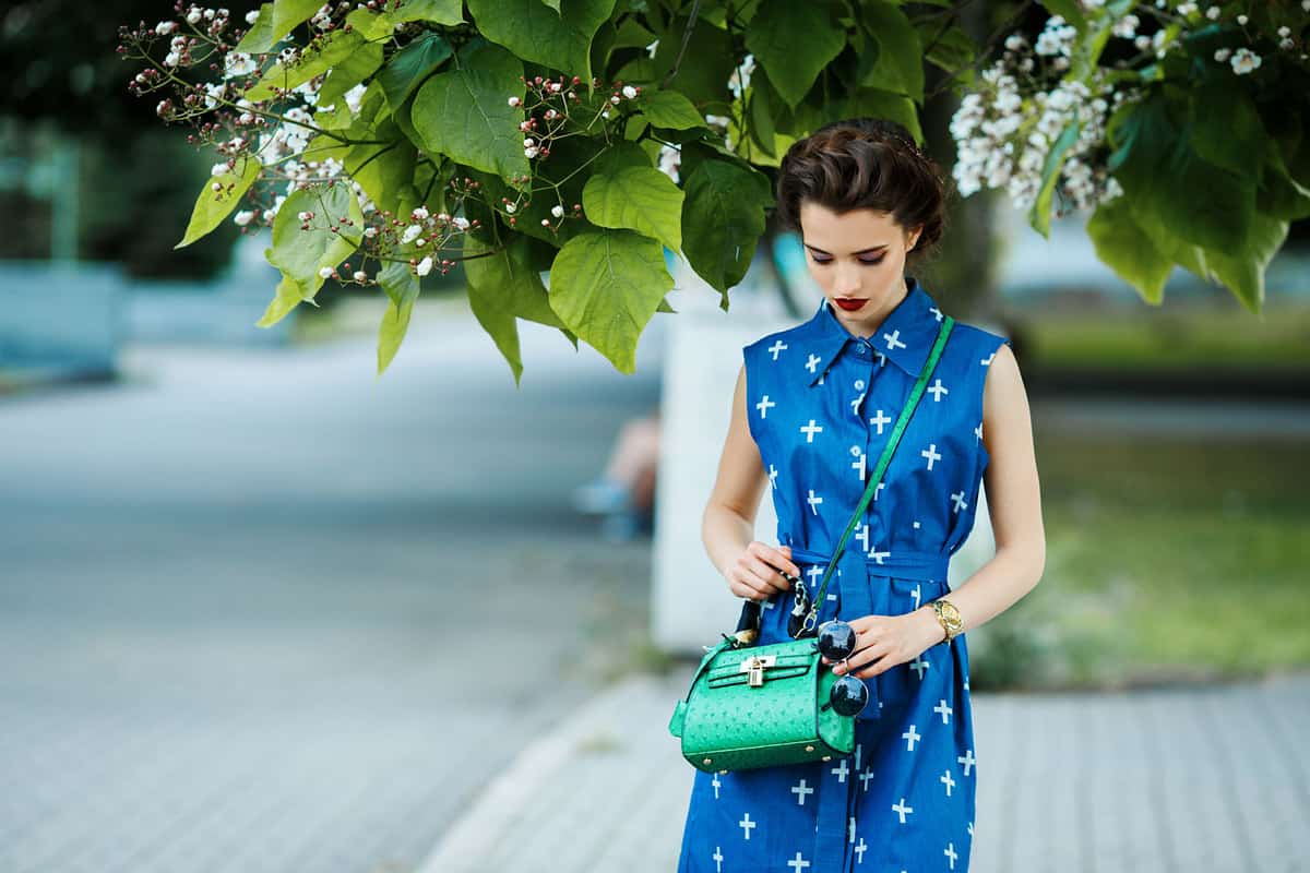 A beautiful woman wearing a blue dress and wearing a matching green bag