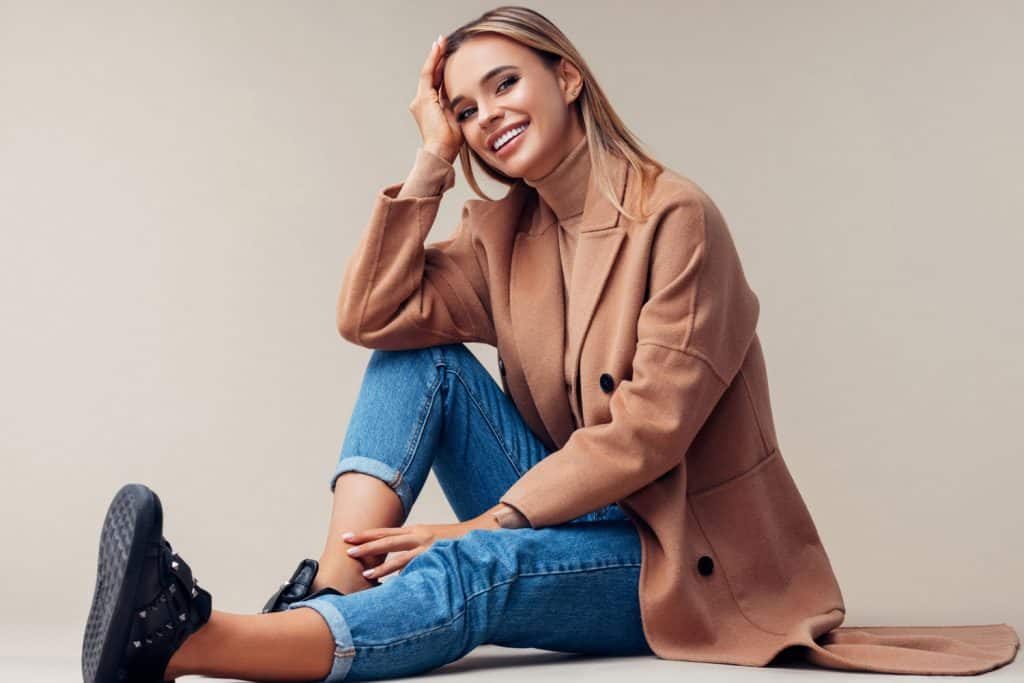 A smiling blonde woman wearing denim jeans and a beige jacket, What Color Accessories Go With A Beige Dress?