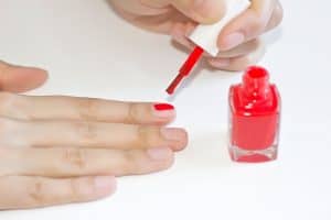 Woman applying red nail polish by herself, Can You Put Regular Nail Polish Over Gel, Polygel, Or Dip Powder?