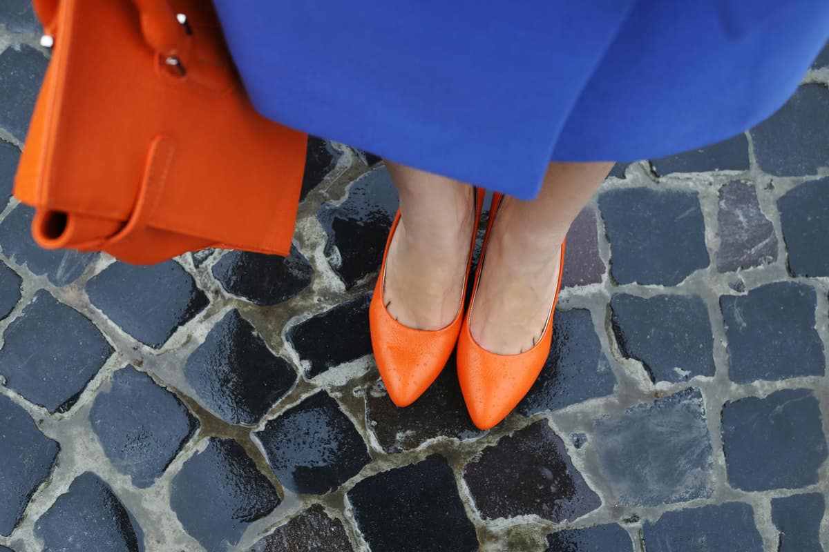 Woman wearing orange shoes and a matching blue dress holding her orange bag