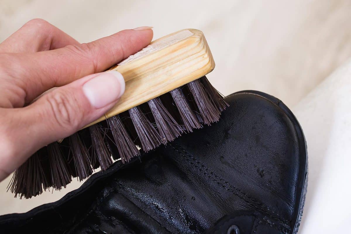 Brush for cleaning shoes in hand and black shoes