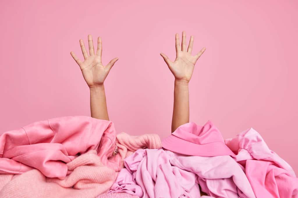 Female hands raised up from pile of unfolded pink clothes