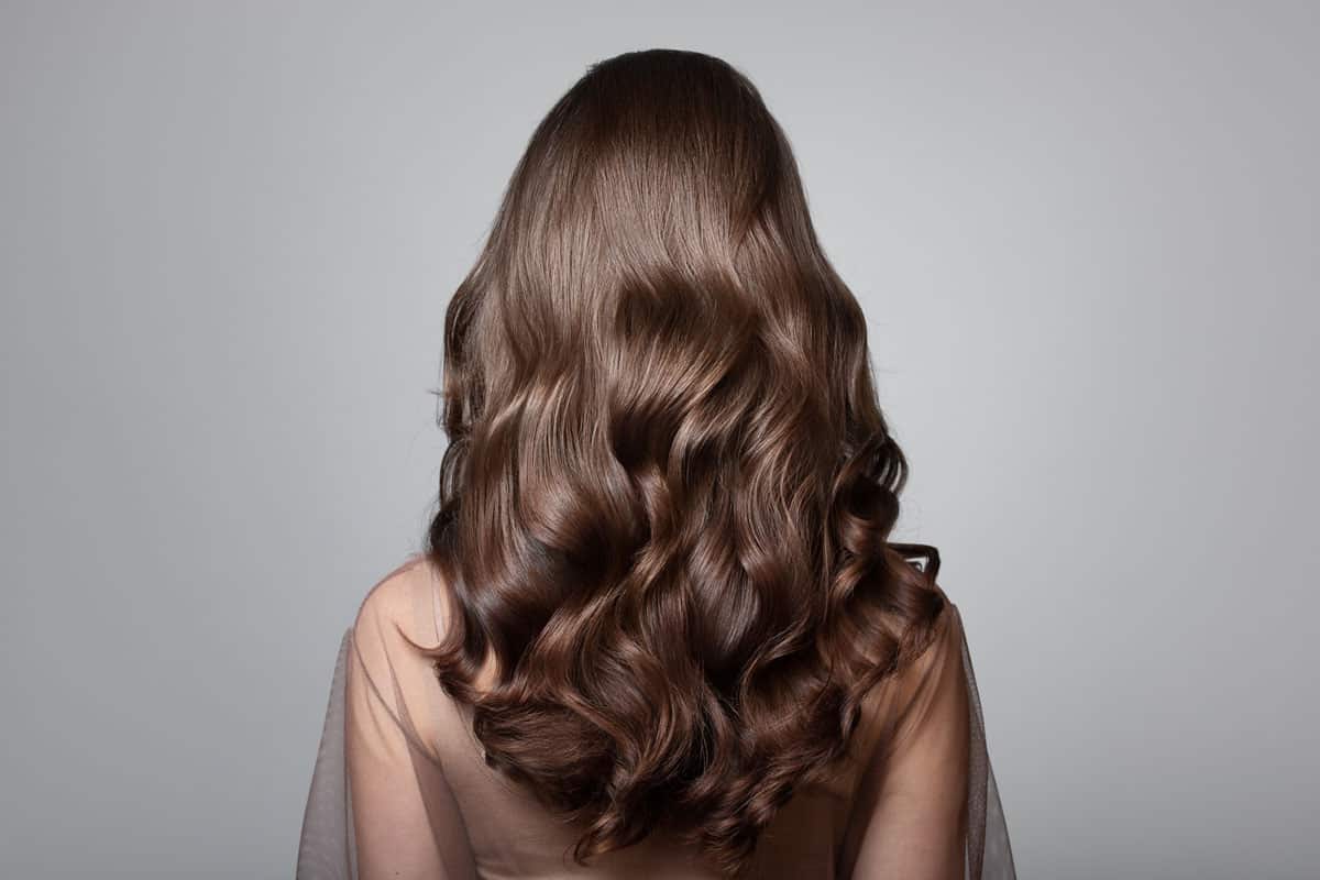 A brunette woman showing her shinny gorgeous hair as a demonstration of heat-free curls.