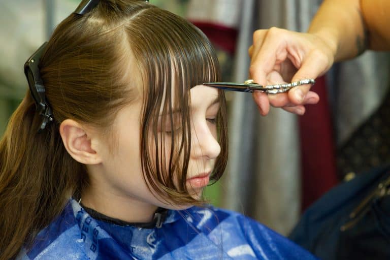 Hairdresser making a hair style to cute little girl. The girl cuts off the bangs