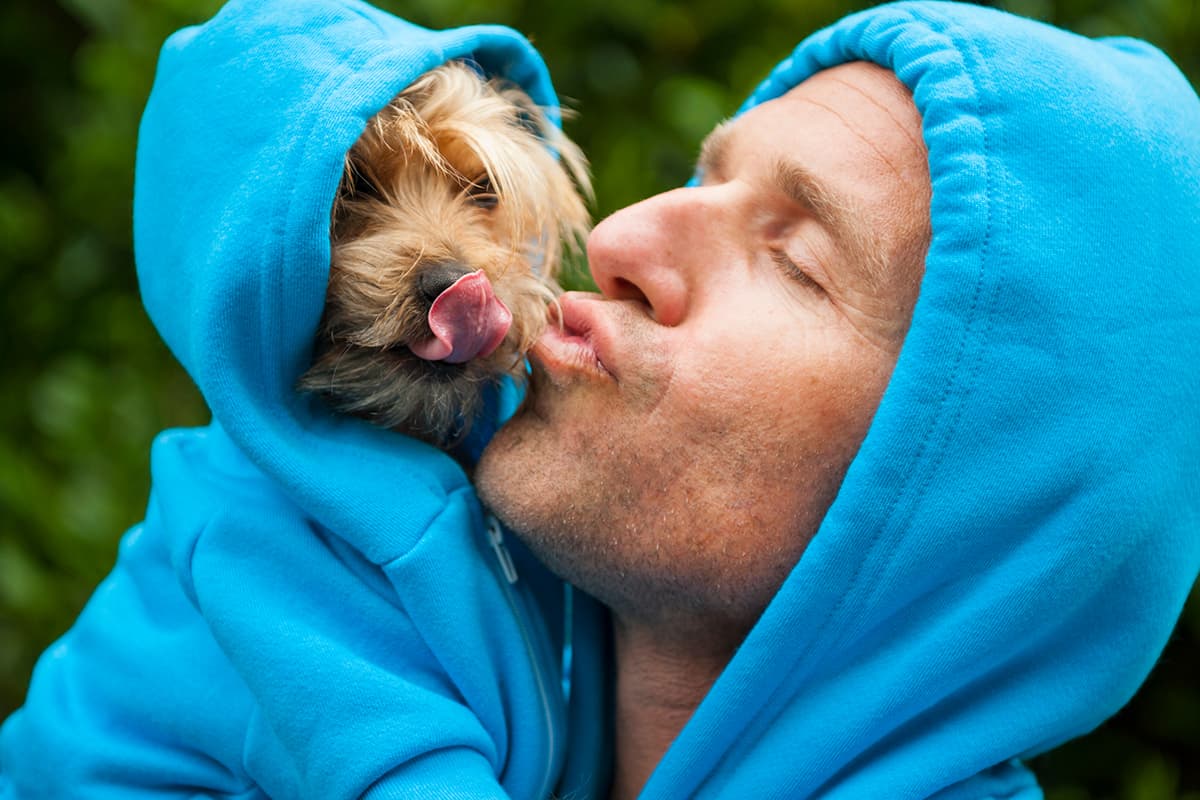 Man kissing his best friend dog in matching blue hoodies