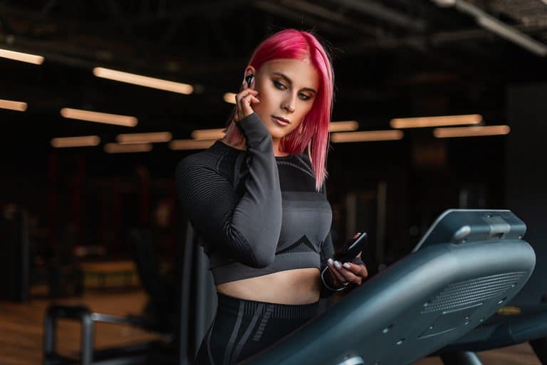 Pretty young fitness model woman with wireless earphone listening to music and running on treadmill, TikTok Star Brings Fashion to the Treadmill: Influencer Recreates Iconic Styles and Goes Viral