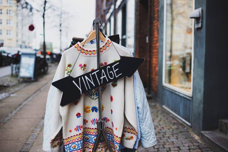 Vintage sign with a background of different vintage clothing on a street, Viral TikToker Brings Grandma's Vintage Wardrobe to Life: The Inspiring Story of Gabi Jones
