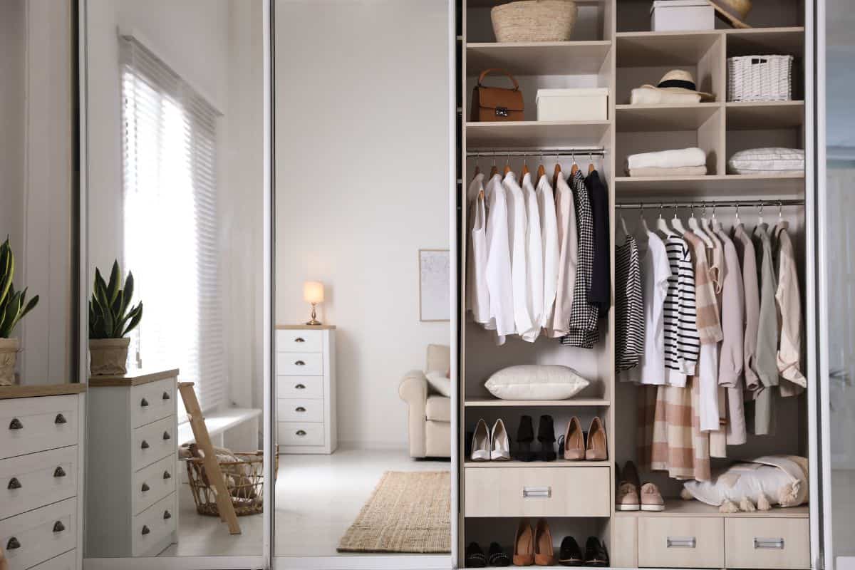 Wardrobe closet with different stylish clothes, shoes and home stuff in room.
