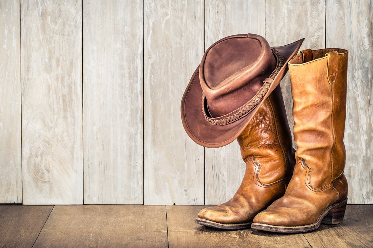 Wild West retro cowboy hat and pair of old leather boots on wooden floor