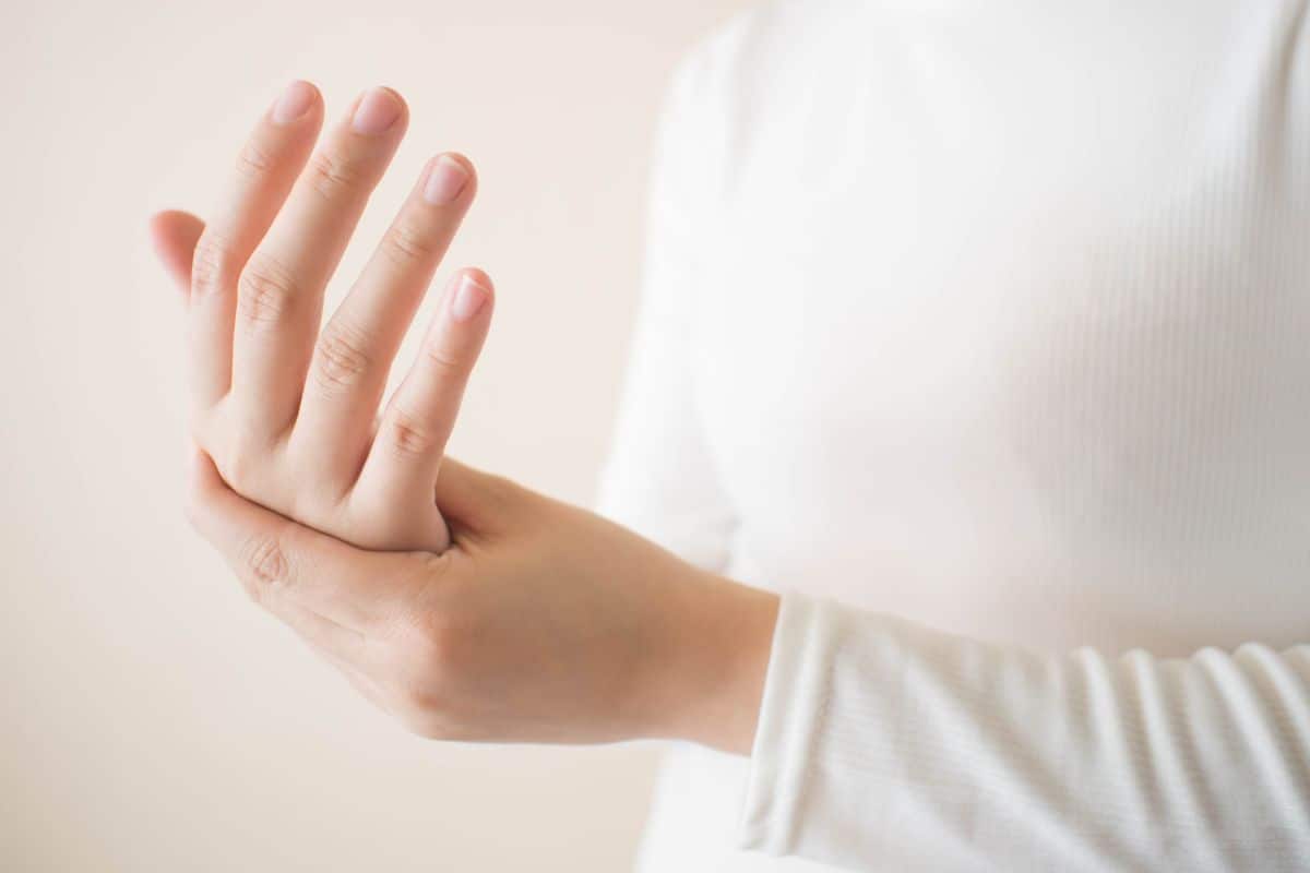 Young female in white t-shirt suffering from pain in hands and massaging her painful hands. Causes of hurt include carpal tunnel syndrome, fractures, arthritis or trigger finger. 