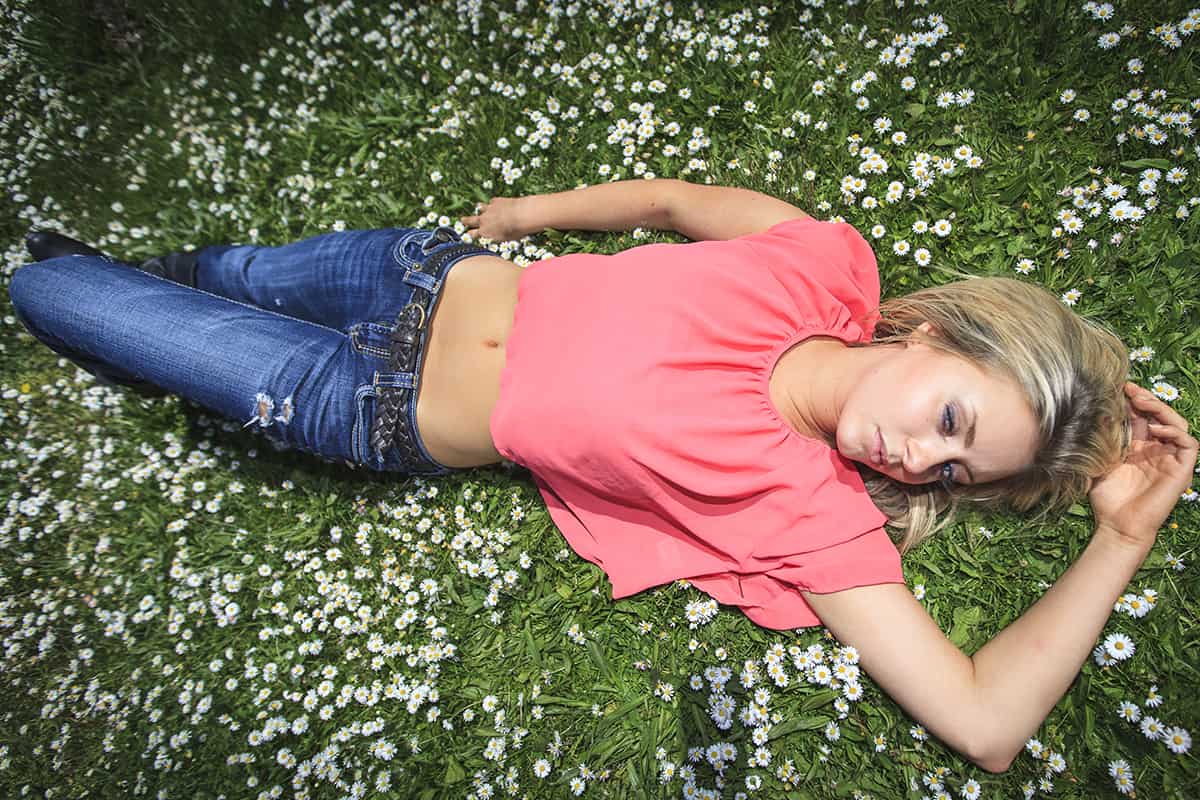 Young woman with blond hair and blue eye posing outside in the park wearing pink shirt and low rise jeans