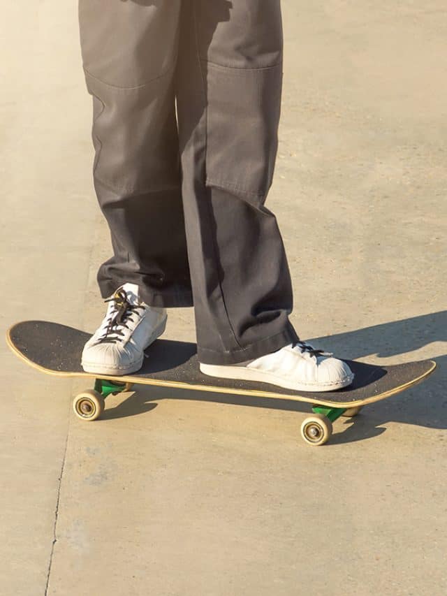 Guy in black cargo jeans and sneakers rides on a concrete floor with a skateboard