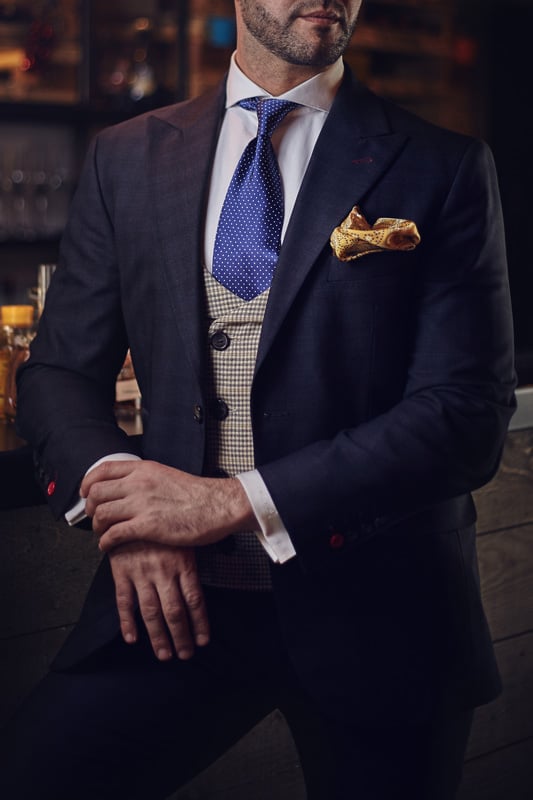 A distinguished gentleman wearing a blue jacket, polka dotted neck tie and gold pocket square
