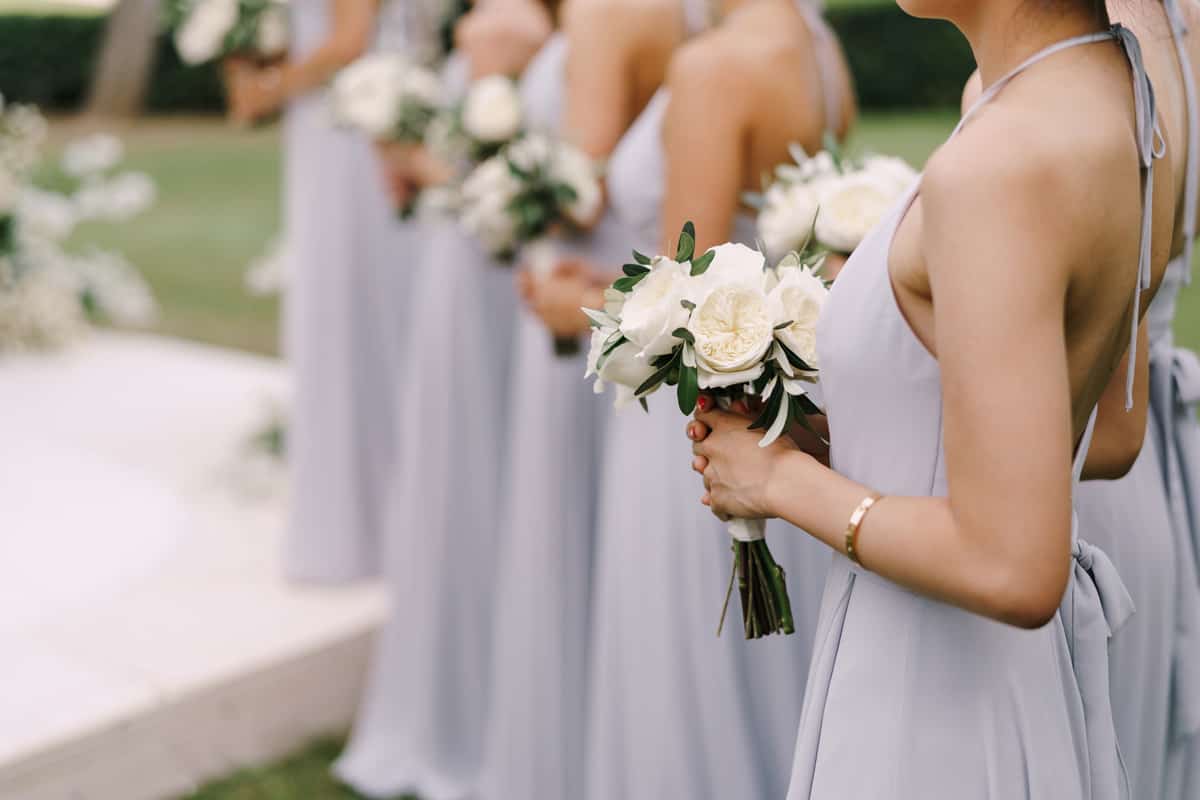 Bridesmaids in dresses stand with bouquets of flowers in a row
