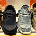 Image of four pairs of hey dude shoes lined up in a row. The colors are brown, black, grey, and tan.