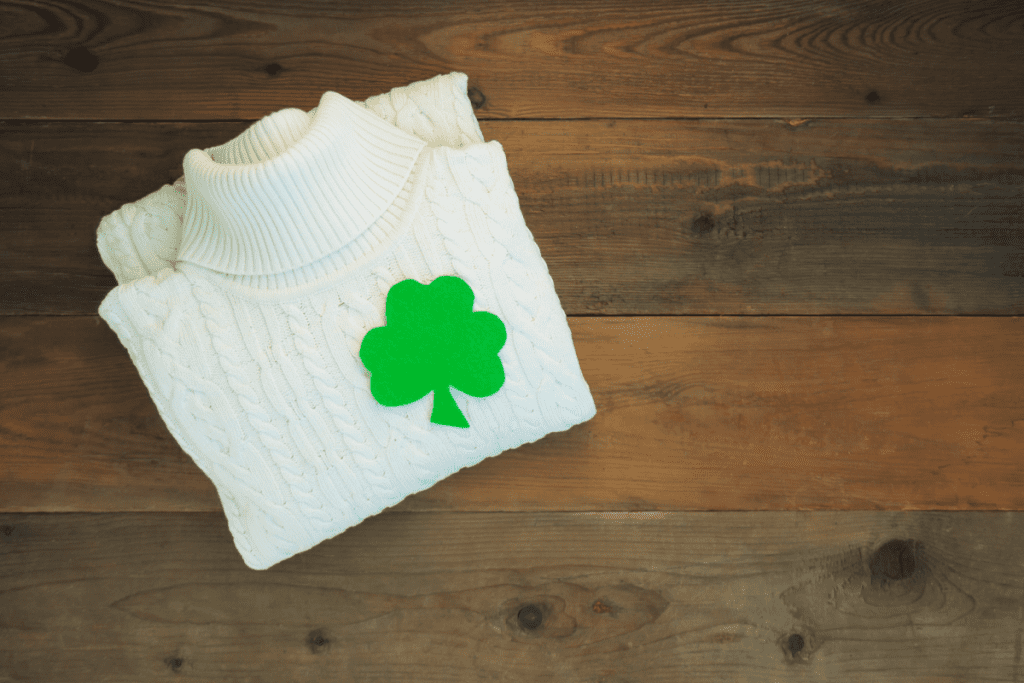 Photo is showing a folded up aran sweater with a four leafed clover sticker on it. 
