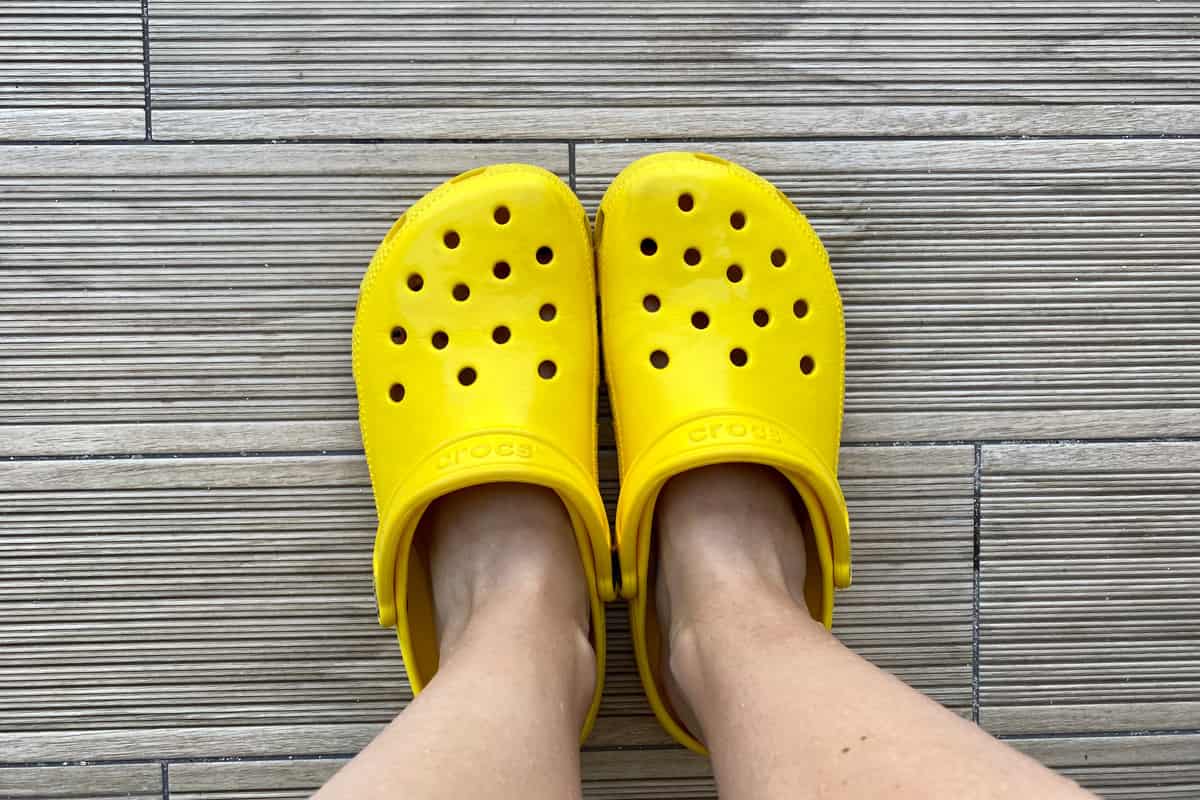 Legs in bright yellow crocs footwear on the grey background