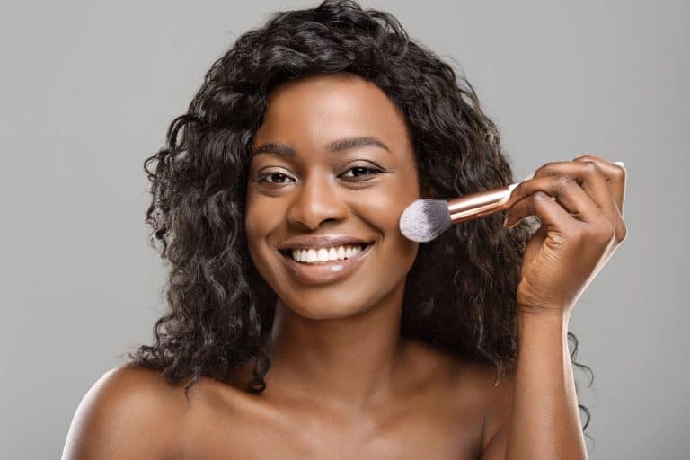 Portrait of pretty afro woman using brush tool, applying blush on face over gray studio background. - Move Over Pink Blush The New Must-Have Makeup Item