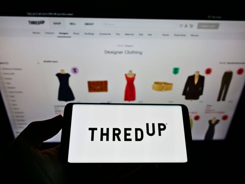 Stuttgart, Germany - 05-23-2021: Person holding smartphone with logo of US fashion resale company ThredUp Inc. on screen in front of website. Focus on phone display. Unmodified photo.

