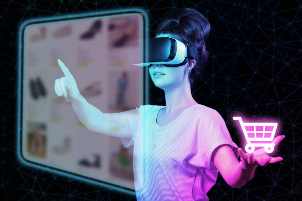 A young woman in VR glasses choice clothes at internet shop point at digital screen, holding neon virtual cart. Dark background. The concept of virtual reality, metaverse fashion and online shopping.
