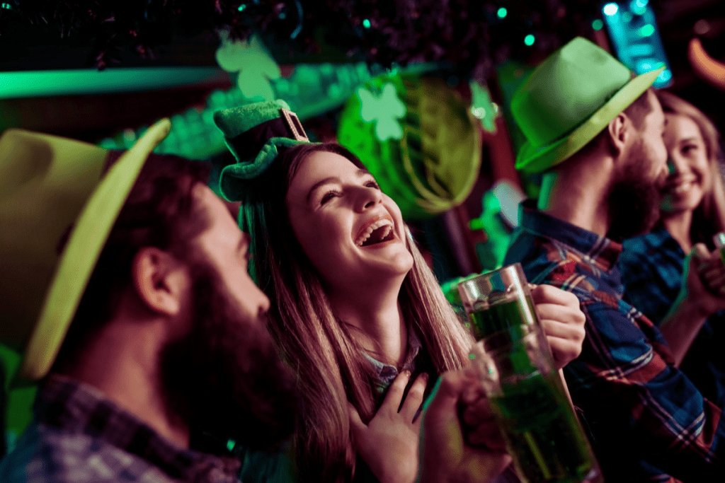 Photo of a crowd having a great time on St. Patrick's Day. They are wearing green hats and laughing.