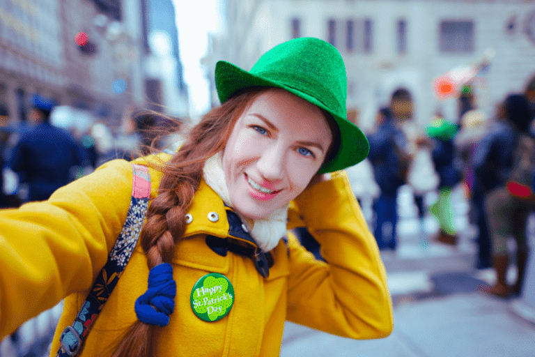 Photo of a woman at a St. Patrick's day outdoor event. In a green hat with a shamrock button on a yellow coat.