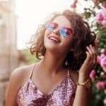 Image of an attractive woman wearing a sequin top and rose colored sunglasses