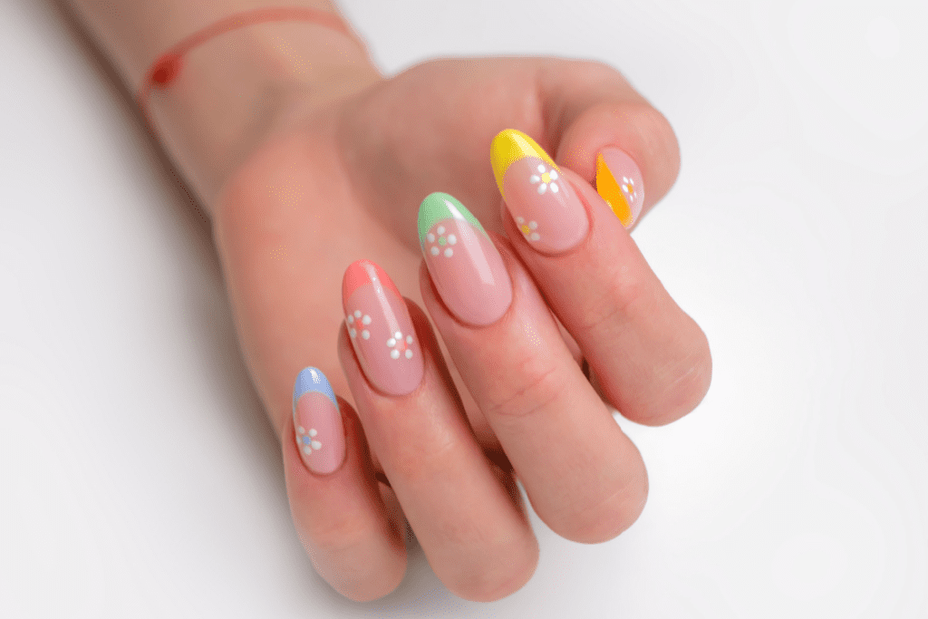 Image of a french manicure featuring multicolored pastels on nail tips with nail art of small white flowers.