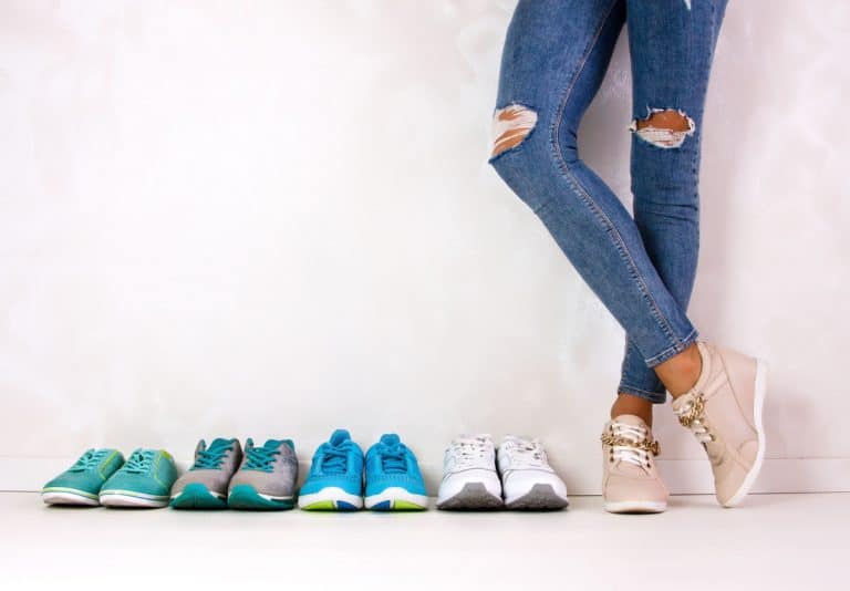 Image of a line of sneakers against the wall with a person wearing skinny jeans and another pair of sneakers.