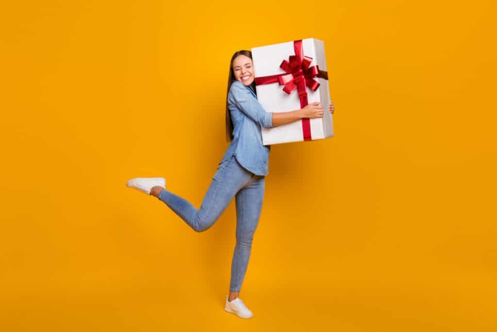 Image of a teenager with an oversized present wrapped with a big bow. 