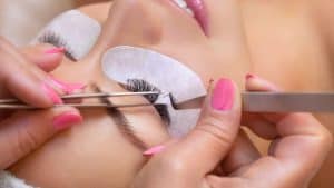 Woman placing eyelashes in her client, How to Get Eyelash Glue Off: Tips and Tricks - 1600x900