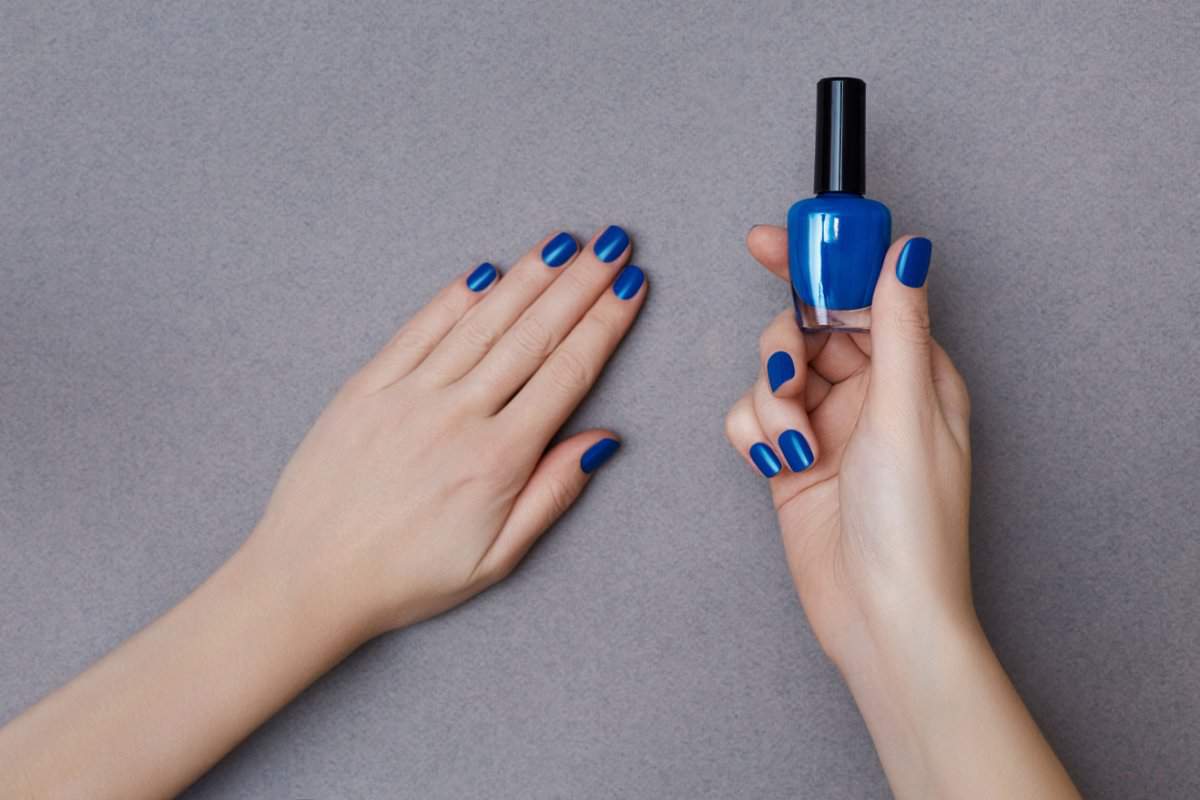 Female hands with manicure in trendy classic blue color holding a bottle of nail polish