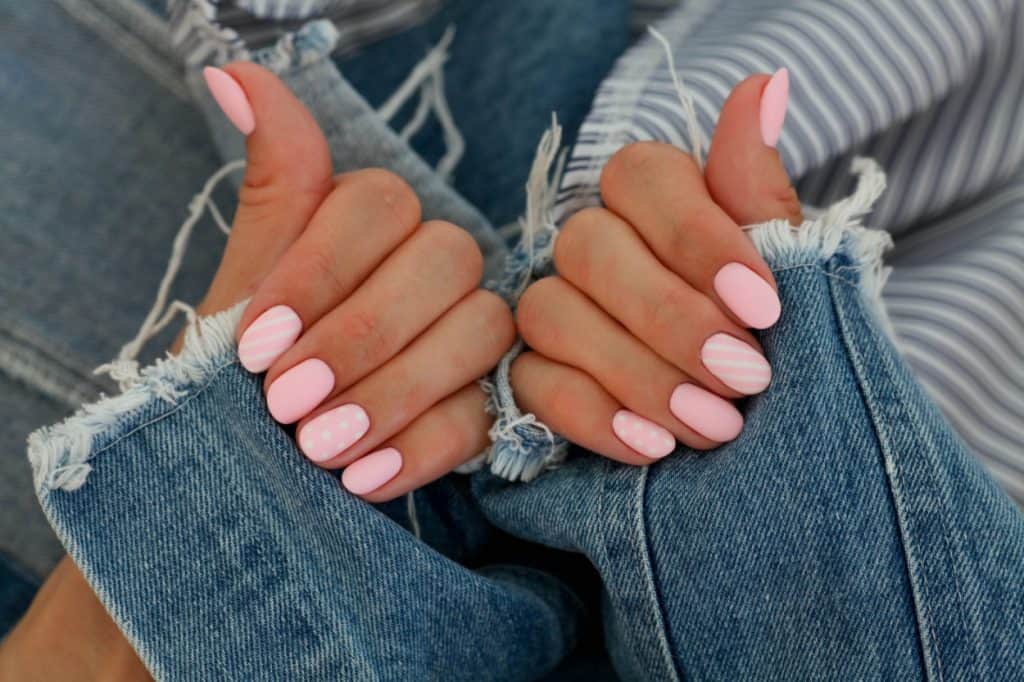 Delicate pink matte oval shaped manicure on jeans background