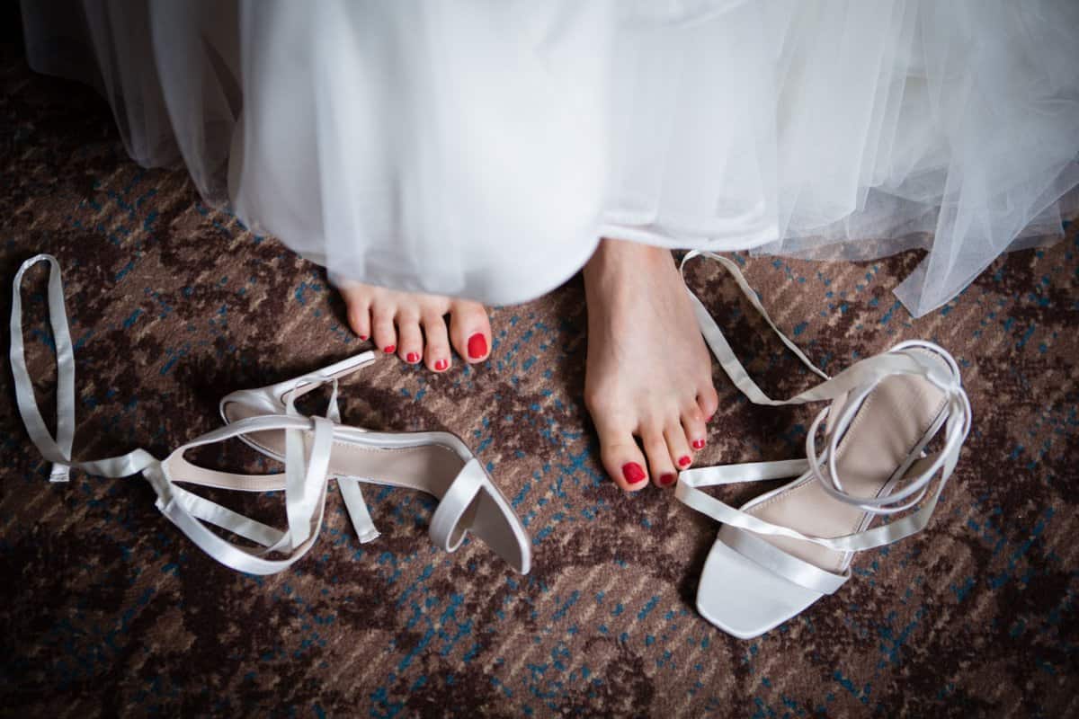 Bride's feet with red nail polish on the toes and bridal high heel white shoes with white ribbon