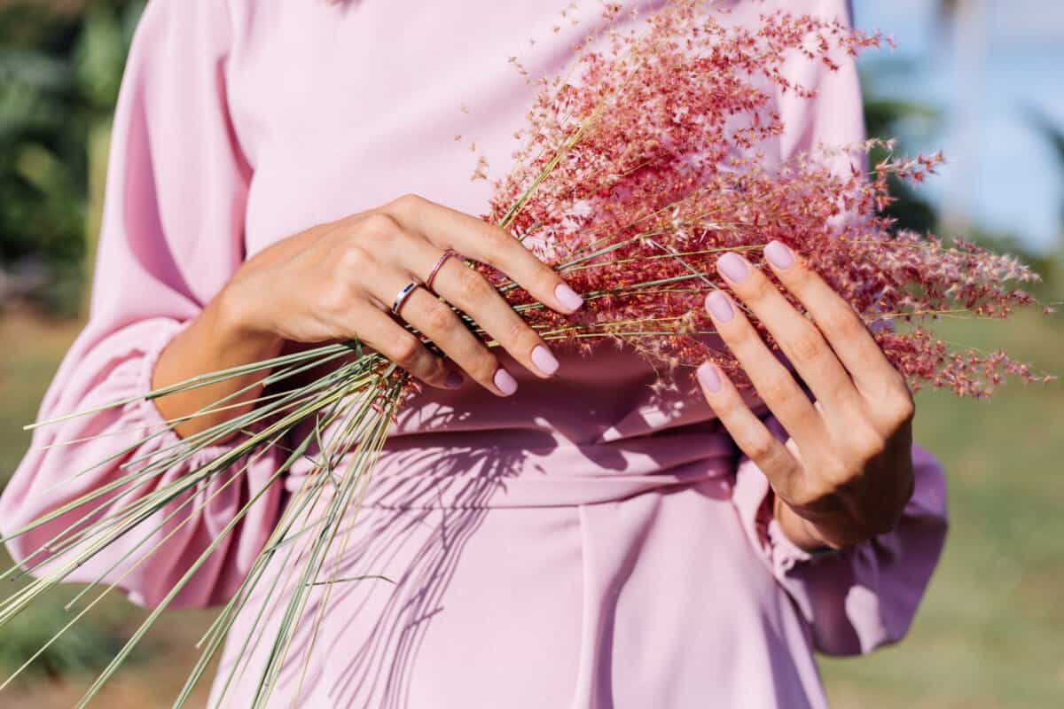 Woman in pink summer dress holding wild flowers with  pink gel polished manicure nails.