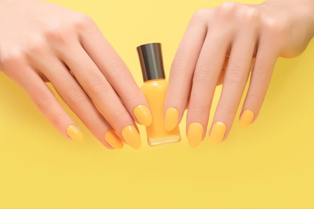 Female hands with yellow nail design. Female hands hold yellow nail polish bottte.