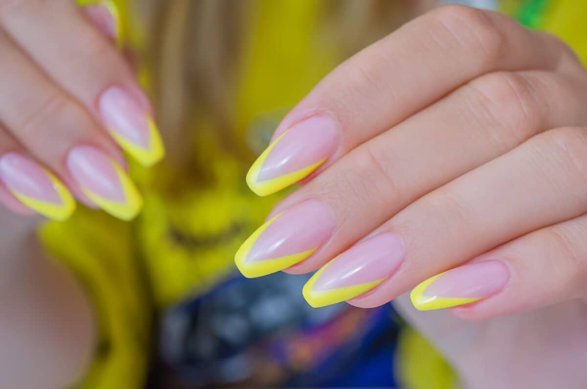 The hand of a young woman with a French manicure of yellow color, nails in the shape of a ballerina
