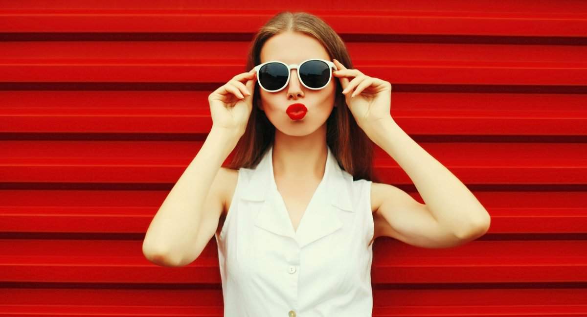 young woman model posing blowing her lips with red lipstick wearing sunglasses